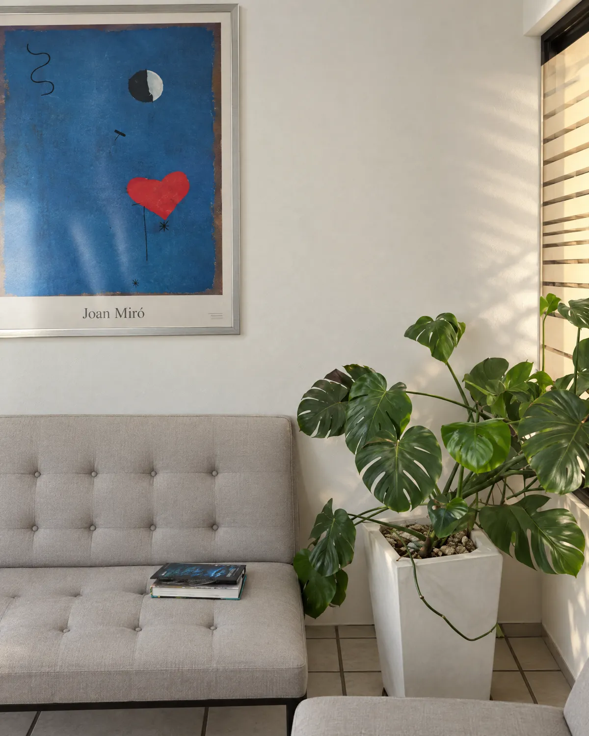 Sala de espera: sillón tapizado, una monstera y un cartel de Joan Miró